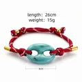 Détail d'un bracelet tressé rouge avec un élément central en acrylique bleu turquoise. - Rouge