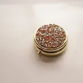 Macro view of portable round metal pillbox with a sparkling rhinestone lid detail - Gold - Silver Champagne Rhinestone