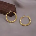 Détail de boucles d'oreilles créoles torsadées dorées sur fond gris textile. - Boucle d'Oreille Mobius Twist (E-070-Or) / Doré