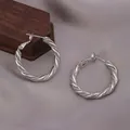Vue détaillée de boucles d'oreilles créoles torsadées Mobius argentées sur fond tissu. - Boucle d'Oreille Mobius Twist (E-070-Platine) / Platine