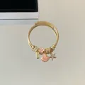 Detailed close-up of gold stainless steel wire bracelet with pink enamel flower charms - Starfish Shell