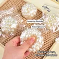 Main pressant un jouet anti-stress spongieux transparent avec perles sur plateau - Balle de Perle Blanche 6cm