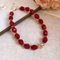Macro detail showing vintage red acrylic beads and a heart-shaped gold pendant on a necklace. - Red
