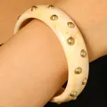 Retro beige tortoise resin bangle with polished gold dome studs worn on a model's wrist - Rivet Style / White