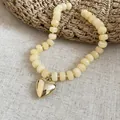 Primo piano di un ciondolo a cuore su una collana di perle acriliche color caramella - Collana / Cachi