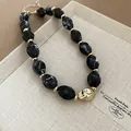 Close-up view of twisted black and white marbled acrylic beads and gold spacers for necklace. - Black
