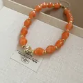 Close-up of orange acrylic beaded necklace with unique gold-tone twisted center bead detail. - Orange