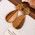 Detailansicht brauner Marmor-Resin-Tropfenohrringe auf rustikalem hellem Stoffhintergrund. - Tropfenform / Braun