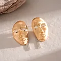 Detailed view of gold mask earrings with silver tassels on stone texture - Earrings / Gold