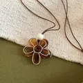 Gros plan sur un pendentif fleur en résine ambre avec bordure argentée et cordon - Marron
