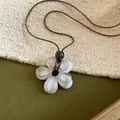 Détail de près d'un pendentif fleur en résine blanche sur un collier en cordon brun - Ivoire
