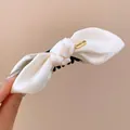 Close-up view of a cream fabric bow hair claw clip with a gold 'classic' metal tag - Twist Clip / White
