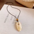 Gros plan d'un collier bohème rétro avec pendentif ovale en résine et texture marbrée - Style Café et Blanc