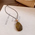 Gros plan détaillé d'un pendentif en résine brune en forme de larme sur cordon cuir - Style Goutte Café