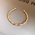 Gedetailleerd vooraanzicht van een elegante goudkleurige gedraaide metalen open armband - Glanzend Gedraaid / Goud