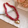 Gros plan d'un collier en perles de résine rouge avec un grand pendentif cœur doré - Rouge