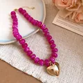 Gros plan d'un collier en perles de résine fuchsia avec un pendentif cœur doré poli - Violet