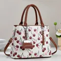 Gros plan sur un sac à main blanc à imprimé cerise avec anses brunes et breloque mini-sac - Blanc Cassé