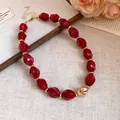 Primo piano di una collana di perle acriliche rosse con una maglia a cuore dorata - Rosso