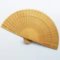 Close-up of a yellow hollowed-out wooden folding fan with intricate carved patterns - 20cm / Gold