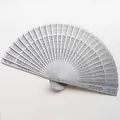 Detail view of an elegant hollowed-out wooden folding fan with intricate floral patterns - 20cm / Silver