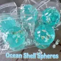 Primer plano de una bola antiestrés con forma de concha marina turquesa en su envase plástico - Bola Concha de Mar (Maltosa) / 6cm
