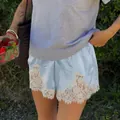 Dettaglio dei pantaloncini in raso azzurro con bordo in pizzo bianco su una modella - Taglia S / Pantaloni e gonne / Blu
