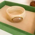 Detail view of a retro cream-colored marble-textured acrylic wide bracelet in a tray. - Vintage Wide Style (HB6269) / Light Coffee