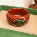 Detailed view of a retro wide acrylic bangle with a green oval stone and gold bezel. - Vintage Wide Style (HB6269) / Red & Dark Green