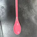 Vibrant pink melamine dessert spoon for milkshakes, displayed on a textured grey surface. - Watermelon red