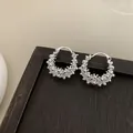 Detailed view of elegant silver textured hollow hoop earrings on a dark wooden surface. - Silver