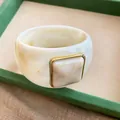 Primo piano di un ampio bracciale in acrilico marmorizzato con dettaglio quadrato dorato. - Bianco Avorio-Cachi