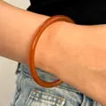 Primer plano de un brazalete de resina color caramelo en la muñeca con textura translúcida. - Brazalete de Círculo Delgado (5007) / Café Oscuro