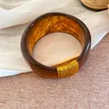 Gros plan d'un large bracelet en résine ambrée marbrée avec des détails en fil doré - Or-Café Foncé