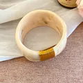 Détail d'un large bracelet en résine marbrée avec un détail élégant de fil doré - Or-Beige