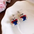 Detailed view of handmade beaded teddy bear earrings with red and blue clothing accents. - Silver Post Jewelry / Silver-White-Blue-Red