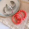 Nahaufnahme von Bohemian-Perlenarmbändern und silbernen Armreifen auf einer gewebten Matte - Mehrteiliges Set / Silber Rosa