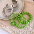 Gros plan de bracelets en perles acryliques vertes et de joncs métalliques argentés sur tapis. - Argent-Vert
