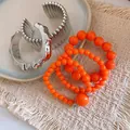 Gros plan de bracelets joncs argentés bohèmes et de bracelets en perles acryliques orange - Argent-Orange