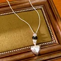 Gros plan d'un collier pendentif cœur en argent mat avec d'élégantes perles noires et argent - Argent