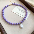 Close-up of purple acrylic beads and baroque pearl pendant on a beige background. - Purple