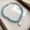 Macro view of light blue acrylic beaded necklace featuring a white baroque pearl pendant. - Blue
