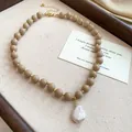 Close-up of beige acrylic beads and iridescent baroque pearl on a canvas tray - Brown