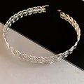 Detailaufnahme eines silbernen geflochtenen Metall-Chokers mit gedrehtem Design. - Gekreuztes Halsband / Silber