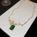 Gros plan d'un collier en or 18 carats avec fleur et zircon vert de forme carrée. - Ensemble Collier + Boucles d'Oreilles / Or-Vert