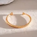 Detailweergave van een goudkleurige C-vormige armband met elegante gedraaide textuur - Schuine Stijl / Goud