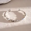 Detailopname van een zilveren gedraaide C-vormige open metalen armband sieraad - Gedraaide Stijl / Zilver