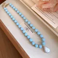Detailed view of a light blue beaded necklace with a large baroque pearl pendant on a tray. - Blue