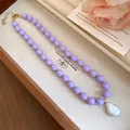 Detailed view of a purple bead necklace with a baroque pearl pendant in a tray. - Purple