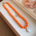 Close-up of orange acrylic beads and a white baroque pearl pendant necklace in a gift box - Orange